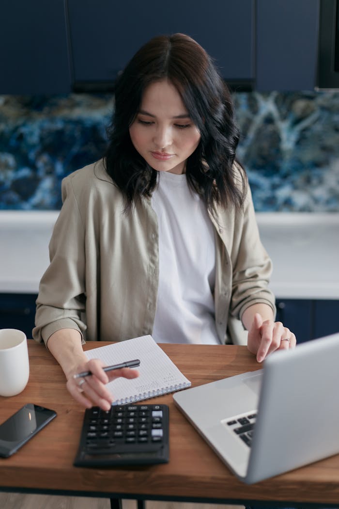 Adult woman working on finances using a laptop and calculator on a wooden table indoors.